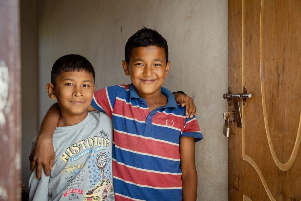 Two young boys smiling. One has his arm around the other's shoulder.