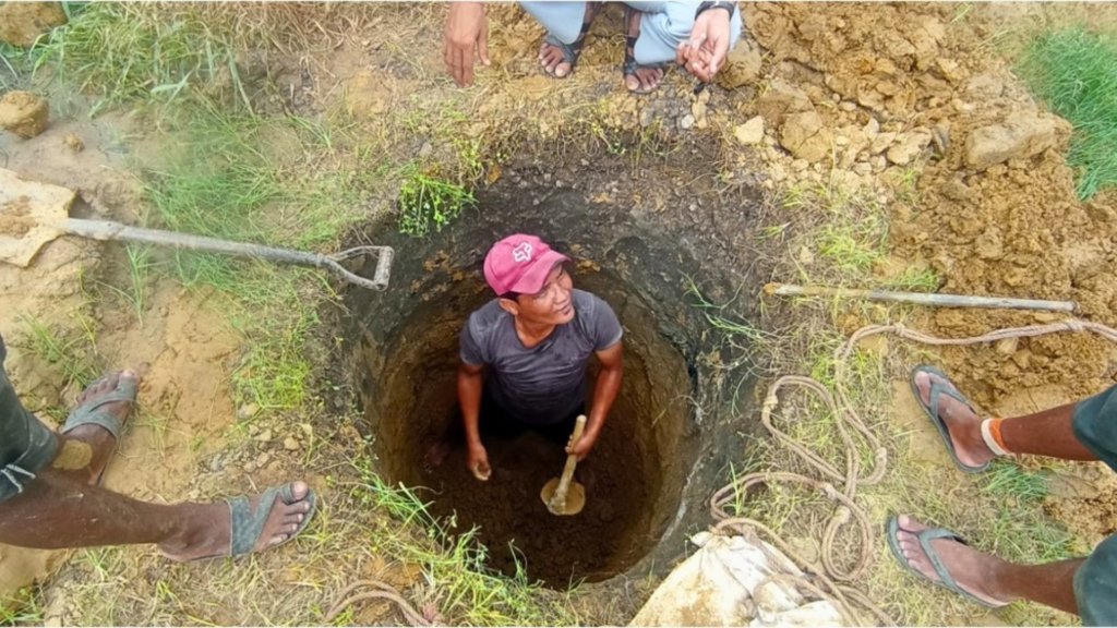 Man in a red cap stands inside a well being dug into the ground.