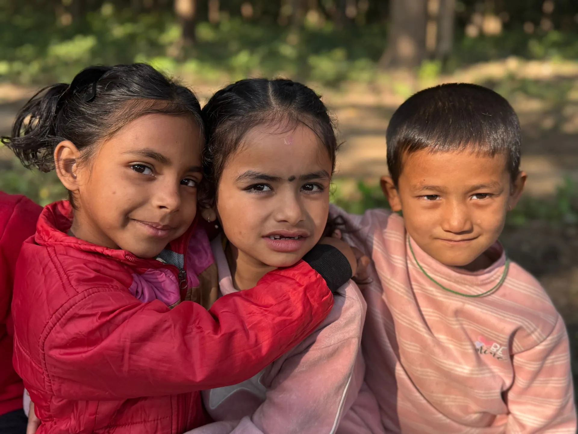 Three young children at RHERI in Nepal hugging and smiling